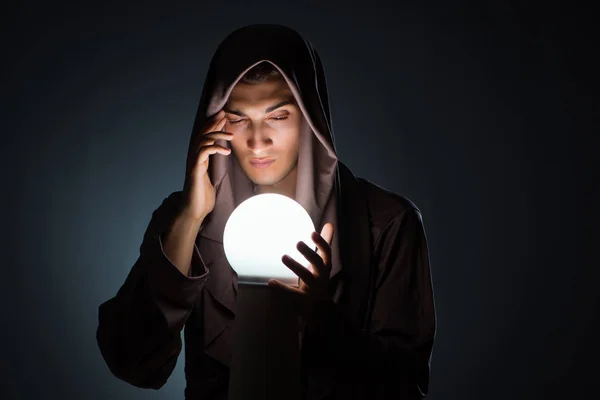 Young wizard with crystal ball in dark room — Stock Photo, Image