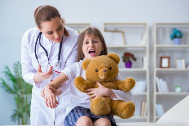 Kadın doktor oyuncak ayıyla küçük tatlı kızı muayene ediyor.