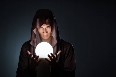 Young wizard with crystal ball in dark room clipart