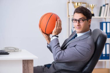 Genç işadamı tatilde ofiste basketbol oynuyor.