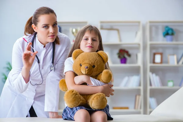 Mujer médico femenino examinando poco linda chica con juguete oso — Foto de Stock