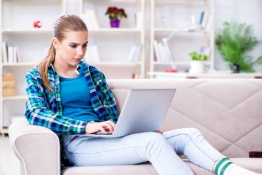 Kanepede dizüstü bilgisayarla oturan bir kız öğrenci.