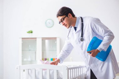 Erkek çocuk doktoru bebek yatağının yanında muayene etmeye hazırlanıyor.