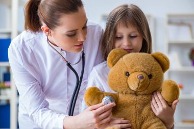 Kadın doktor oyuncak ayıyla küçük tatlı kızı muayene ediyor.