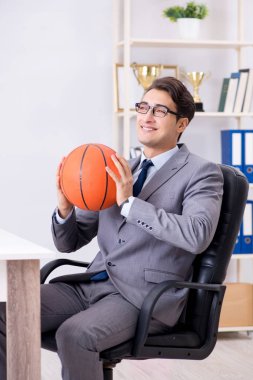 Genç işadamı tatilde ofiste basketbol oynuyor.