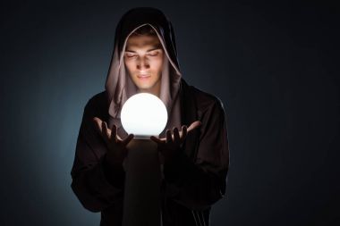 Young wizard with crystal ball in dark room clipart