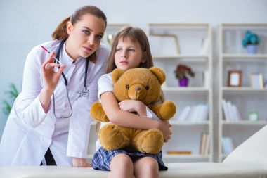 Kadın doktor oyuncak ayıyla küçük tatlı kızı muayene ediyor.