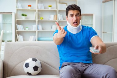 Boynundan sakatlanan bir adam evde futbol maçı izliyor.
