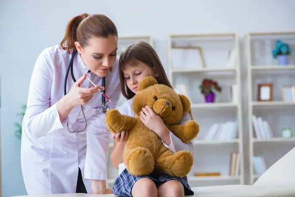 Mujer médico femenino examinando poco linda chica con juguete oso —  Fotos de Stock