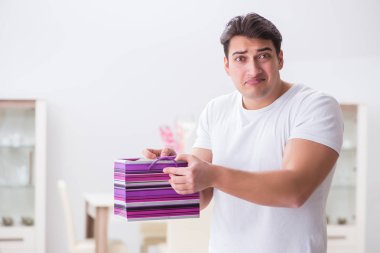 Evde hediye çantası taşıyan genç bir adam karısına sürpriz hazırlıyor.