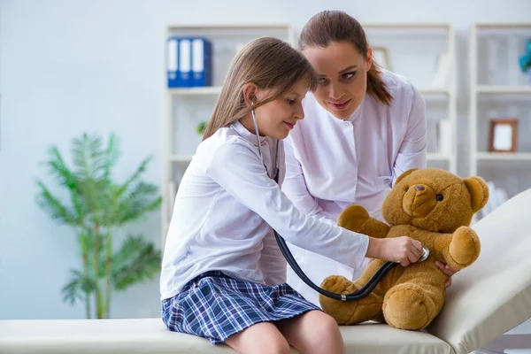 Femme médecin féminin examinant petite fille mignonne avec ours jouet — Photo