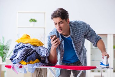 Genç adam evde çamaşır ütülüyor.