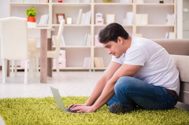 Evde, halı döşemesinde dizüstü bilgisayarda çalışan bir adam.