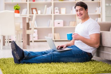 Evde, halı döşemesinde dizüstü bilgisayarda çalışan bir adam.