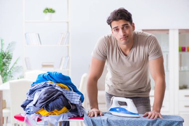 Genç adam evde çamaşır ütülüyor.