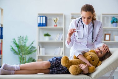 Kadın doktor oyuncak ayıyla küçük tatlı kızı muayene ediyor.