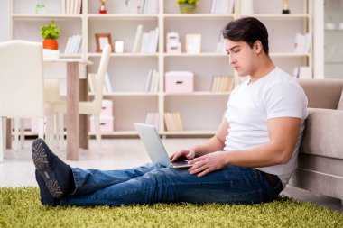 Evde, halı döşemesinde dizüstü bilgisayarda çalışan bir adam.