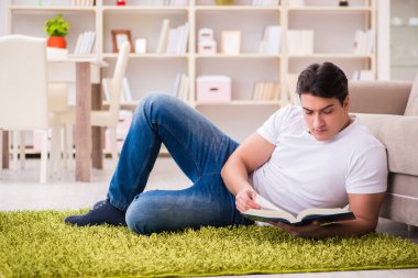 Adam evde yerde kitap okuyor.