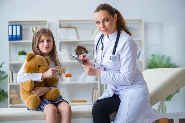 Mujer médico femenino examinando poco linda chica con juguete oso — Foto de Stock