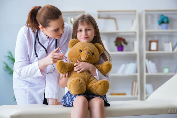 Mujer médico femenino examinando poco linda chica con juguete oso — Foto de Stock