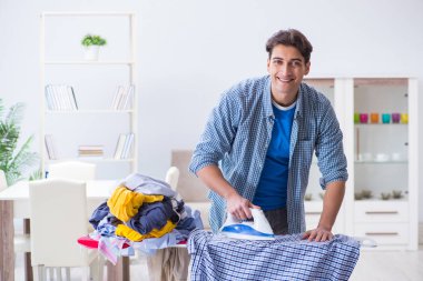 Genç adam evde çamaşır ütülüyor.