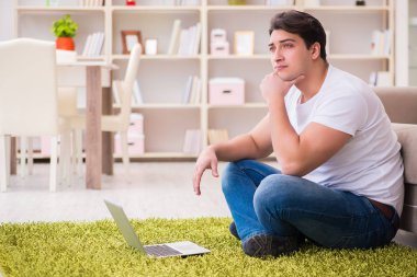 Evde, halı döşemesinde dizüstü bilgisayarda çalışan bir adam.