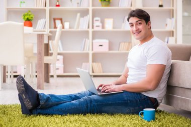 Evde, halı döşemesinde dizüstü bilgisayarda çalışan bir adam.