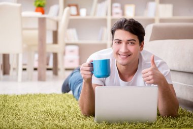 Evde, halı döşemesinde dizüstü bilgisayarda çalışan bir adam.