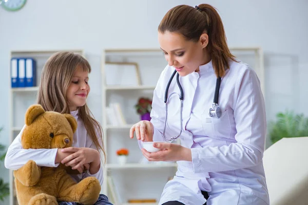 Vrouw vrouwelijke arts onderzoeken klein schattig meisje met speelgoed beer — Stockfoto