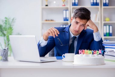 Genç işadamı ofiste tek başına doğum gününü kutluyor.