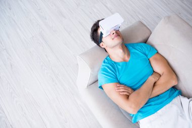 VR gözlüklü genç adam kanepede dinleniyor.