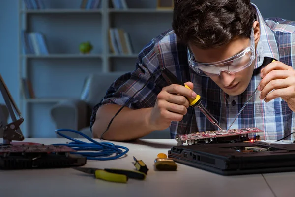 Young repair technician soldering electrical parts on motherboar