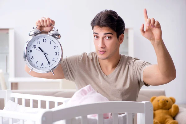 Papá joven con reloj cerca de la cuna recién nacida — Foto de Stock