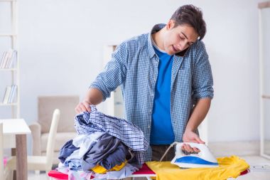 Genç adam evde çamaşır ütülüyor.