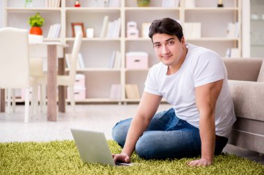 Evde, halı döşemesinde dizüstü bilgisayarda çalışan bir adam.