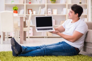 Evde, halı döşemesinde dizüstü bilgisayarda çalışan bir adam.