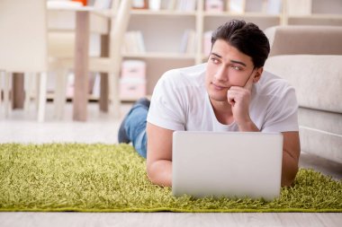Evde, halı döşemesinde dizüstü bilgisayarda çalışan bir adam.