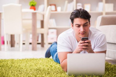 Evde, halı döşemesinde dizüstü bilgisayarda çalışan bir adam.