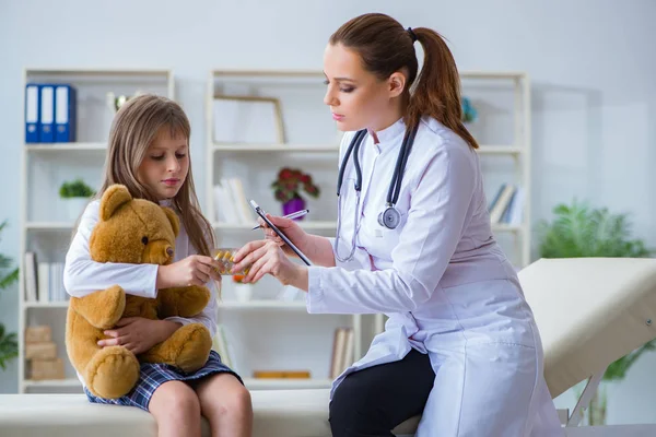 Mujer médico femenino examinando poco linda chica con juguete oso —  Fotos de Stock