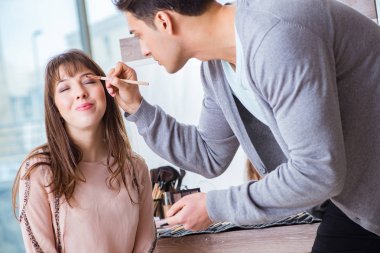 Güzellik salonunda güzel bir kadın için makyaj yapan adam.