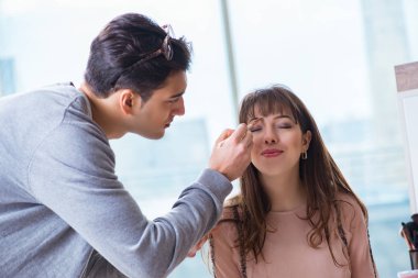 Güzellik salonunda güzel bir kadın için makyaj yapan adam.