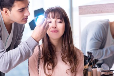 Güzellik salonunda güzel bir kadın için makyaj yapan adam.