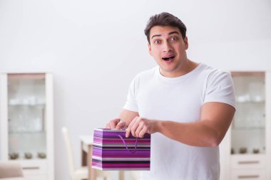 Evde hediye çantası taşıyan genç bir adam karısına sürpriz hazırlıyor.