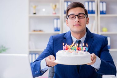 Genç işadamı ofiste tek başına doğum gününü kutluyor.
