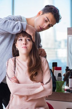 Erkek stilisti bir kadınla güzellik salonunda çalışıyor.