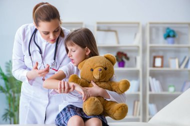 Kadın doktor oyuncak ayıyla küçük tatlı kızı muayene ediyor.