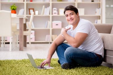 Evde, halı döşemesinde dizüstü bilgisayarda çalışan bir adam.