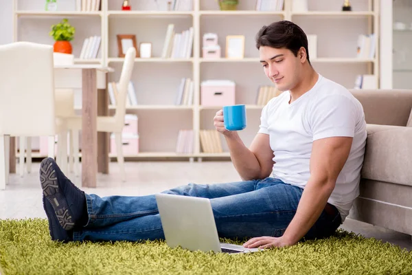 Uomo che lavora sul computer portatile a casa sul pavimento del tappeto — Foto Stock