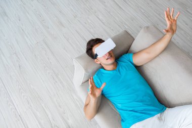 VR gözlüklü genç adam kanepede dinleniyor.
