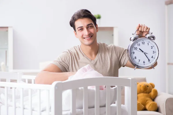Yeni doğmuş bebek yatağının yanında saati olan genç bir baba. — Stok fotoğraf